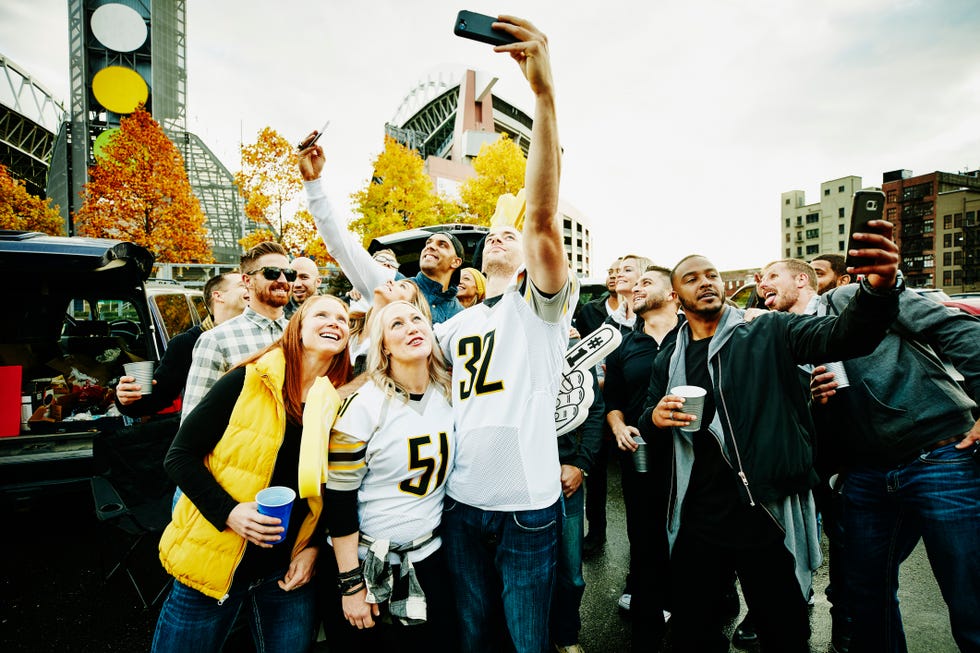 group of friends taking selfies in stadium parking lot before football game