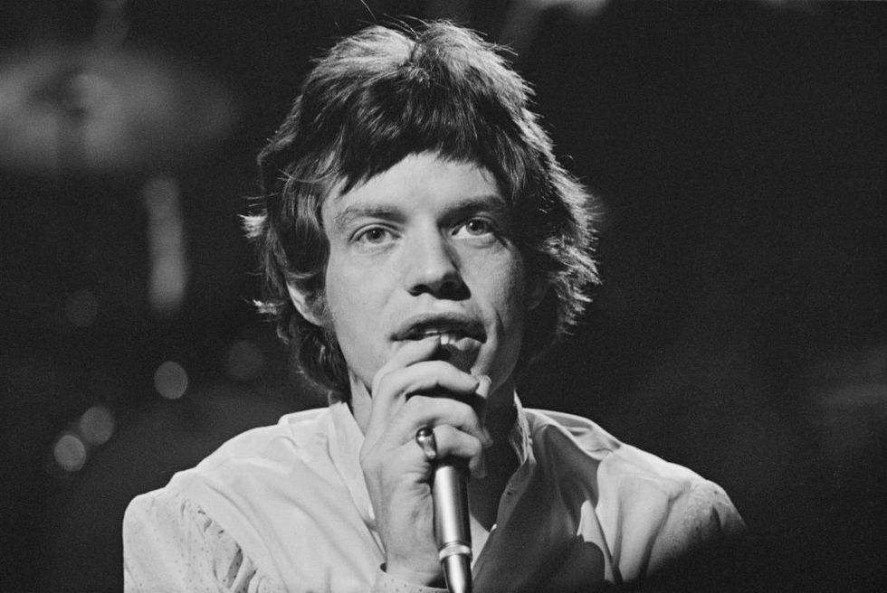 mick jagger holding a microphone to his face during a live performance on a tv show