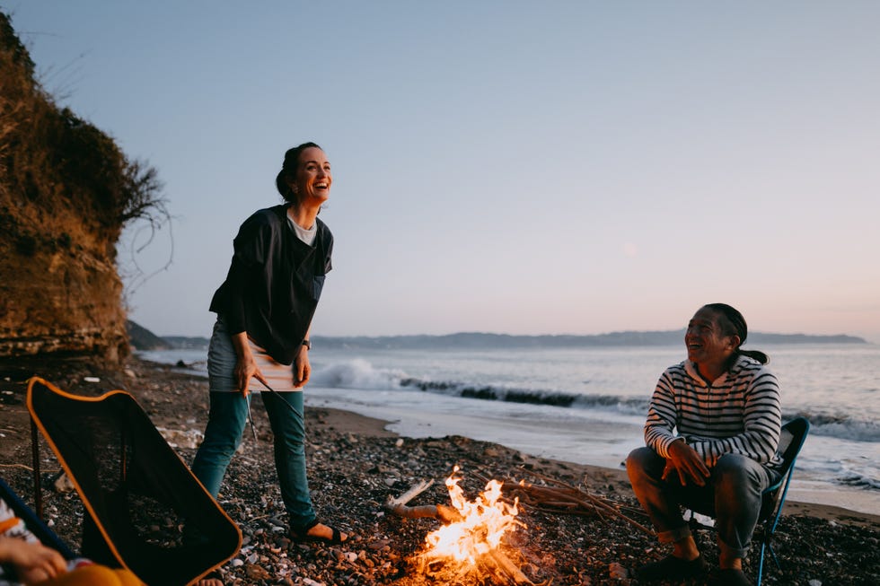 enjoying sunset campfire at beach, two adults play celebrity, a good housekeeping pick for best camping activity