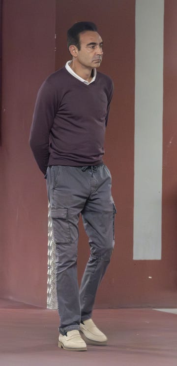 el torero con un jersey de pico en tonor morados y pantalon gris de bolsillos