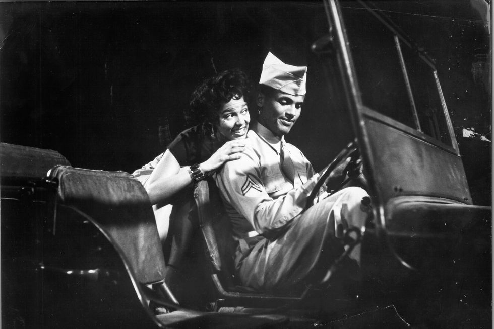 dorothy dandridge and harry belafonte sit in a car while acting in the movie carmen jones, belafonte is wearing a military uniform in the driver seat and dandridge is behind him in the back seat