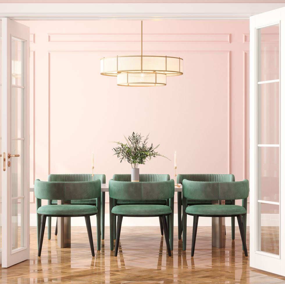 entrance of dining room with dining table, green velvet chairs and pink wall in background