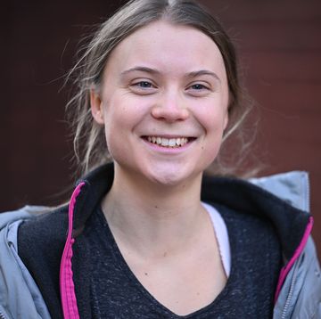 a young woman smiles as she looks left, she wears a light purple coat, black zip up sweater and black shirt