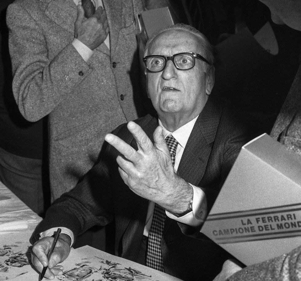 enzo ferrari looking up toward a camera while signing papers with his right hand