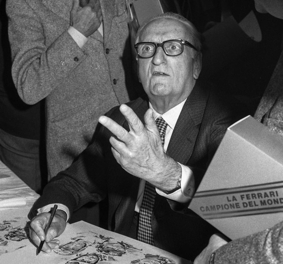 enzo ferrari looking up toward a camera while signing papers with his right hand