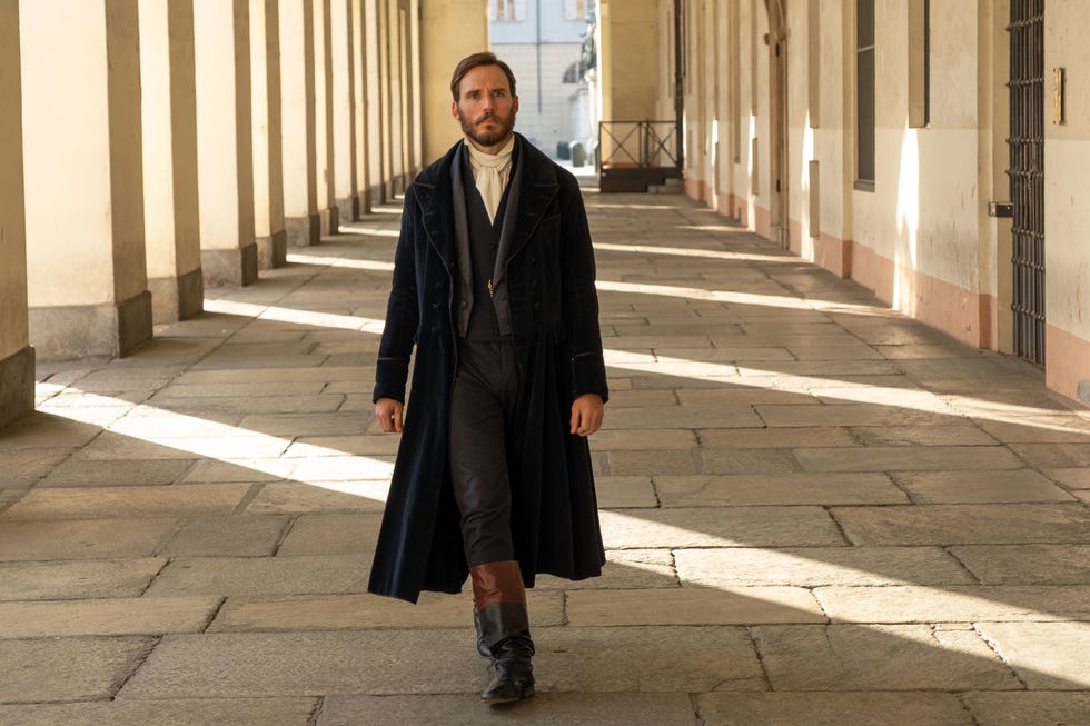 a person walking down a cobblestone corridor with columns