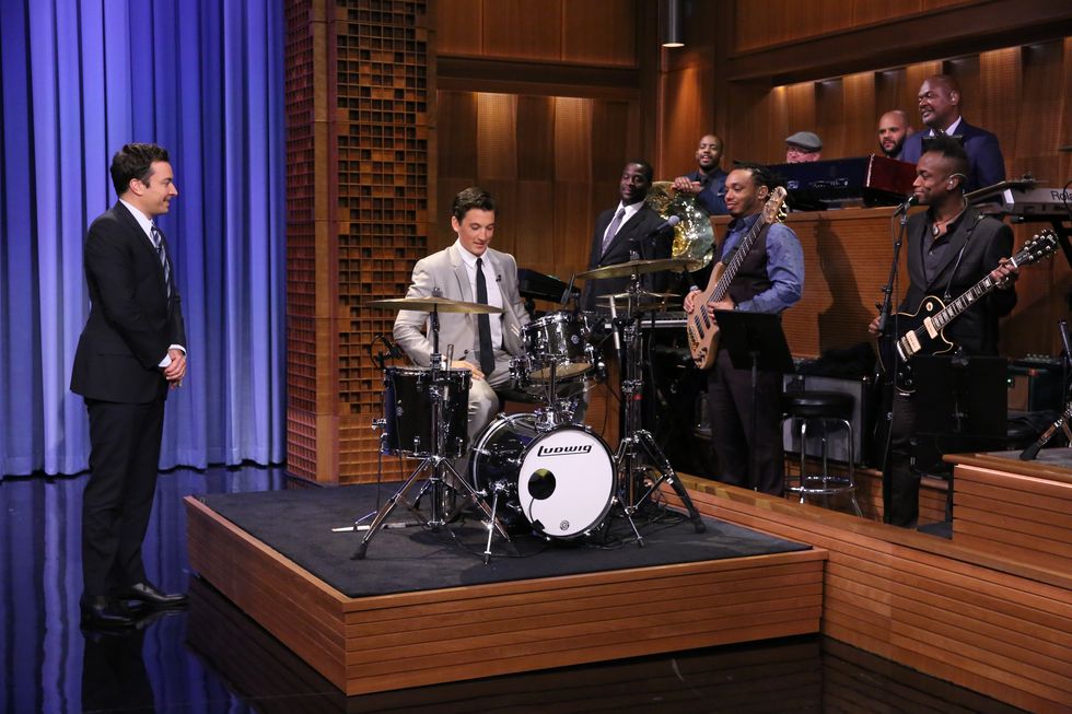 miles teller drums as jimmy fallon stands to the left and musicians watch on the right