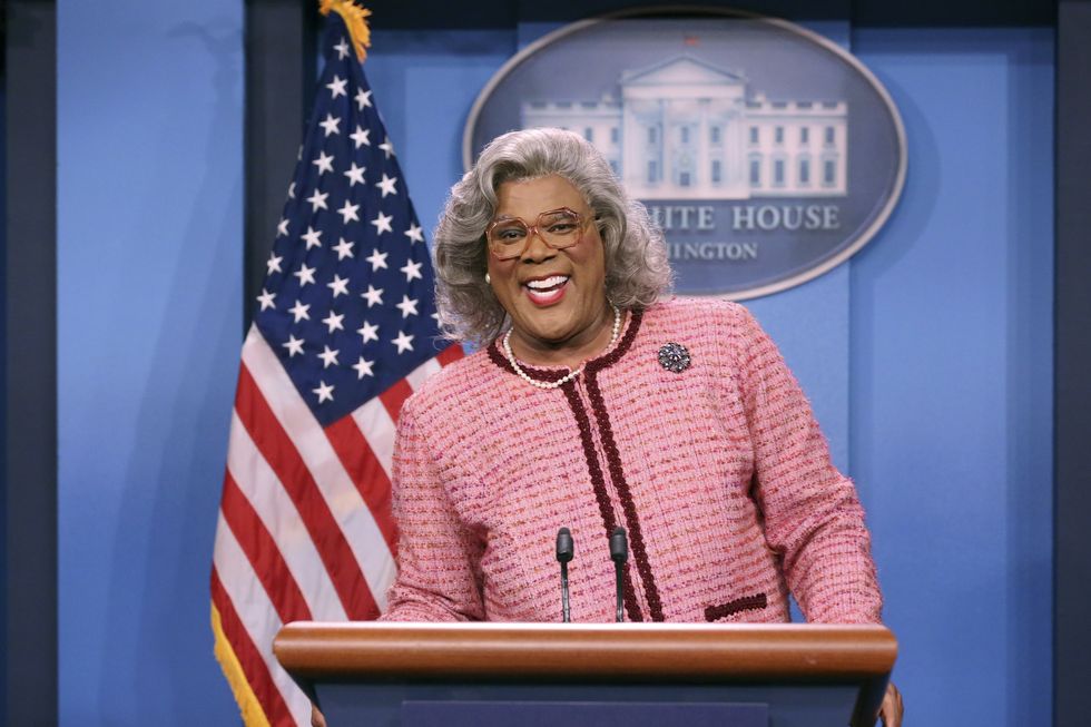 man dressed like a grandmother smiling as she stands behind a podium