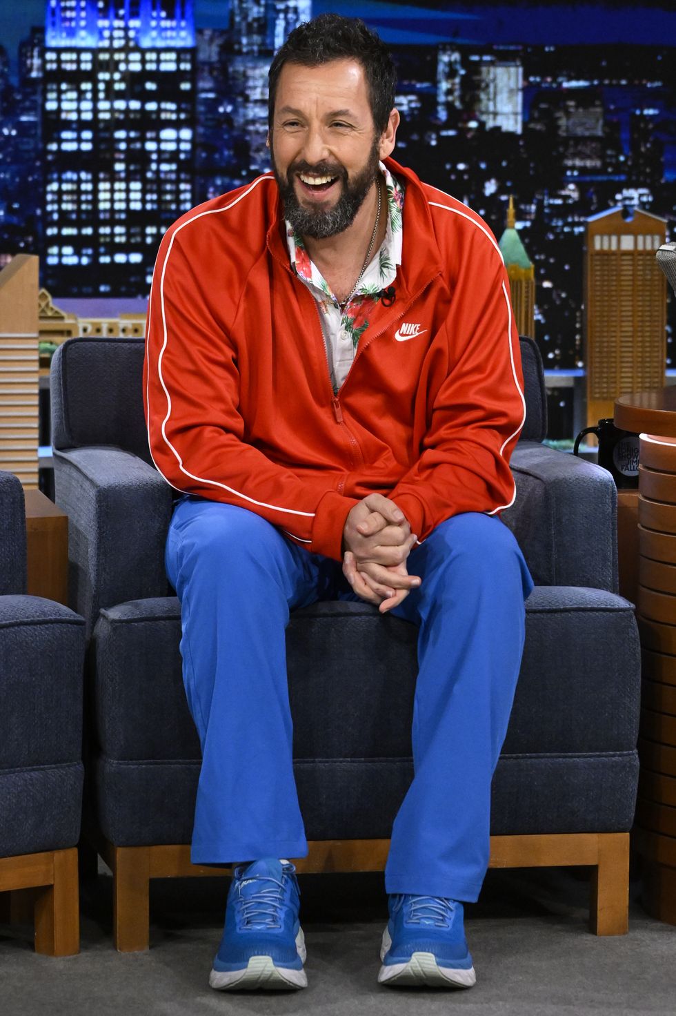 adam sandler smiling and looking toward the audience while sitting for a talk show appearance