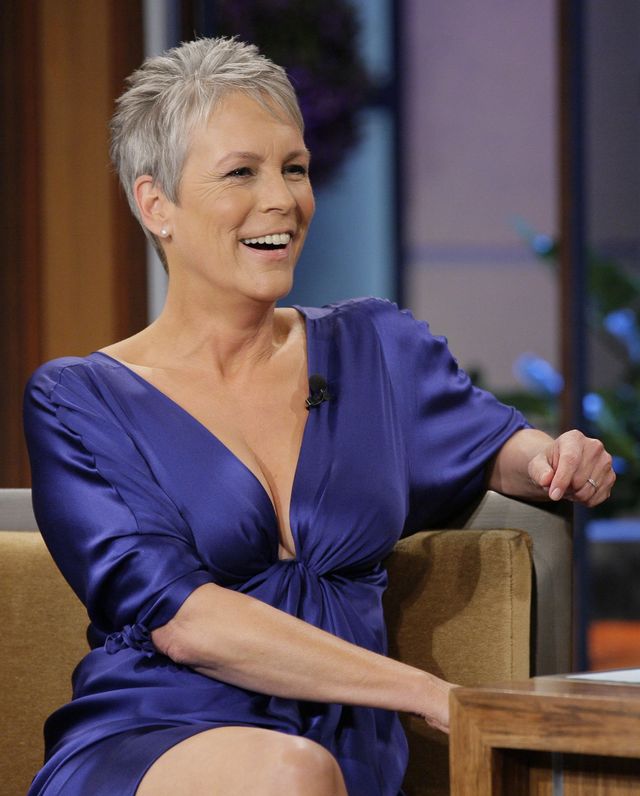 jamie lee curtis wearing a purple dress, smiling and sitting at a chair next to a desk on a television set