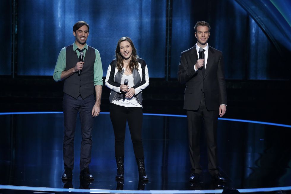 michael palascak, taylor tomlinson, and anthony jeselnik stand on a stage smiling, each holds a wireless microphone in one hand