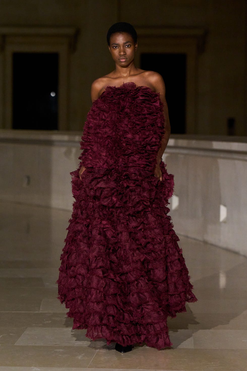 A model wearing a voluminous burgundy dress with ruffled layers