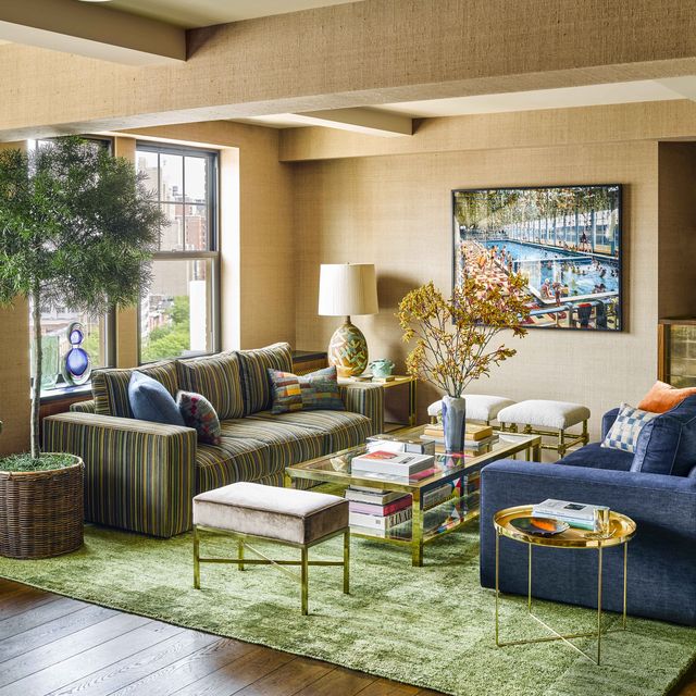 living room with green velvet rug and seating area with striped green sofa and a large blue armchair across it and a two tier gold and glass cocktail table filled with books and objects