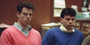 erik menendez and lyle menendez inside a wood paneled room, erik wears glassed and a salmon colored sweater over a green and white striped collared shirt, lyle wears a blue sweater over a yellow and white striped collared shirt