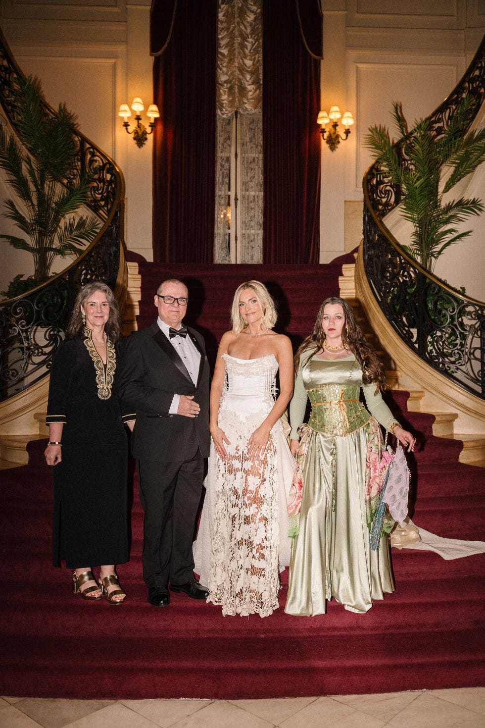 group of four people posing on a grand staircase in elegant attire