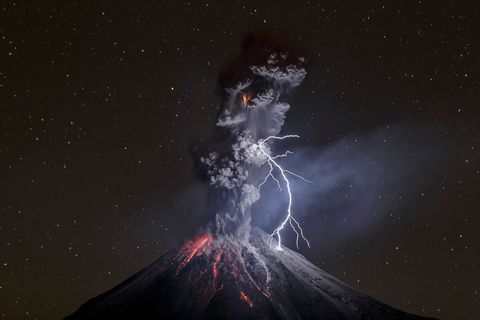 Een bliksemschicht splijt de nachthemel boven de berg Colima terwijl een kolkende aszuil de sterren verhult