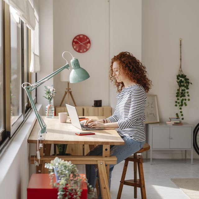 woman sitting on a desk using a laptop computer while working from home business, freelance and home office concept