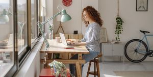 woman sitting on a desk using a laptop computer while working from home business, freelance and home office concept