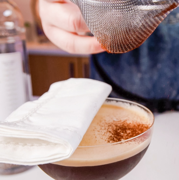 dusting espresso powder over an espresso martini with a paper towel