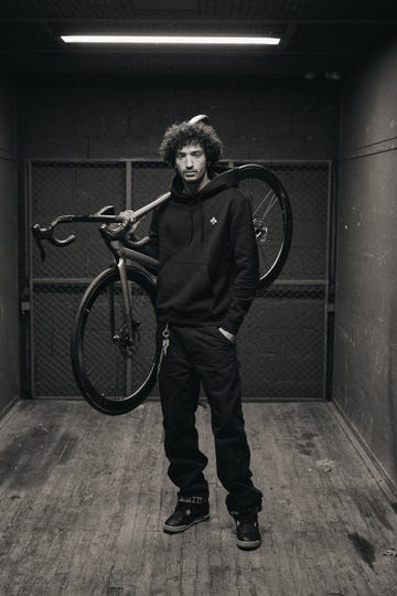 individual standing with a bicycle over their shoulder in a dimly lit space