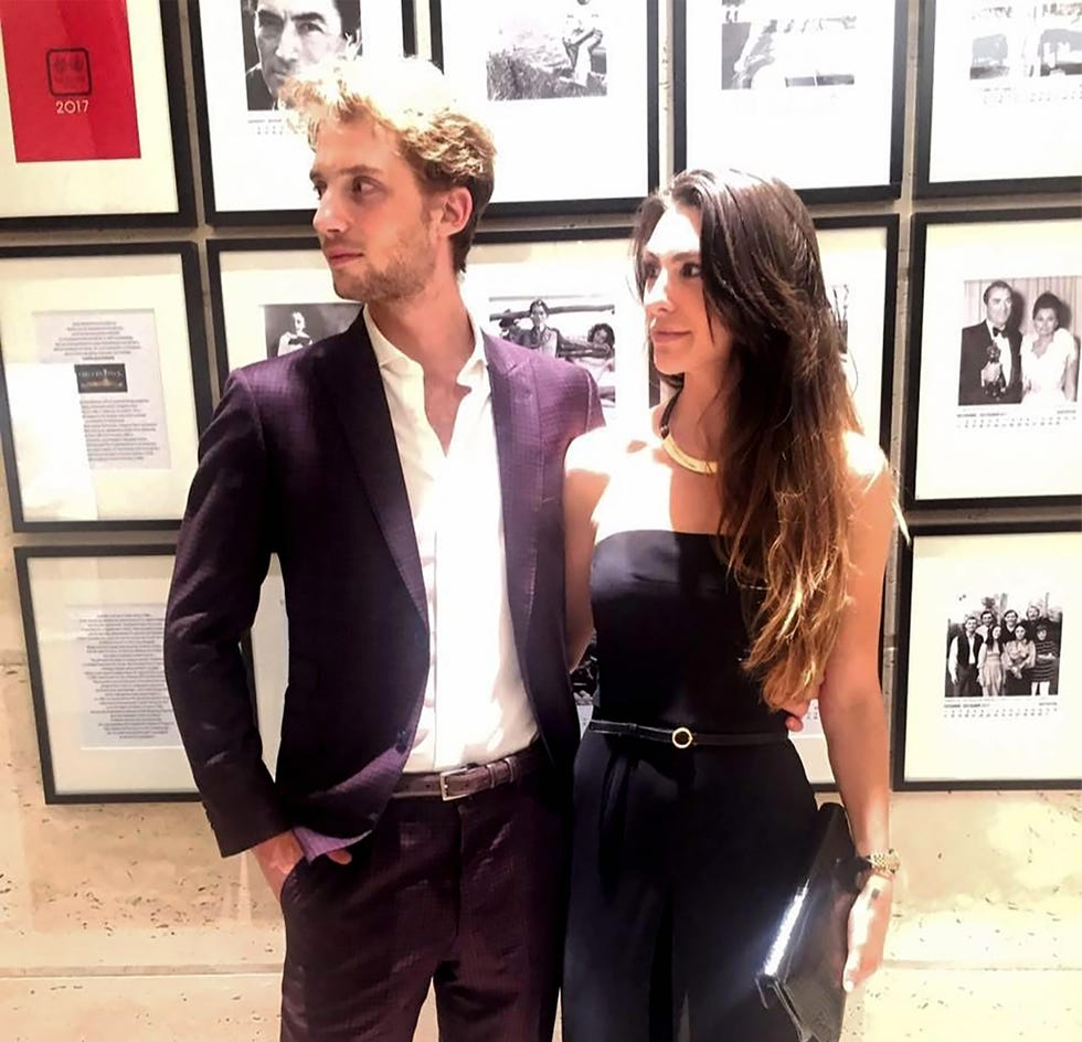 couple standing in front of a wall with framed photographs