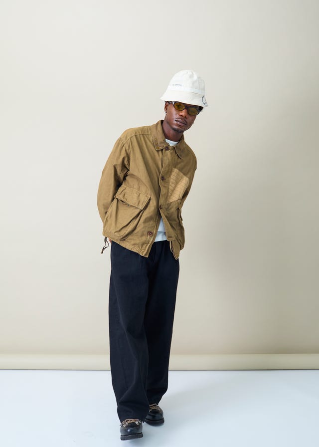 eine Person in einem legeren Outfit mit einer olivgrünen Jacke und einer dunklen Hose