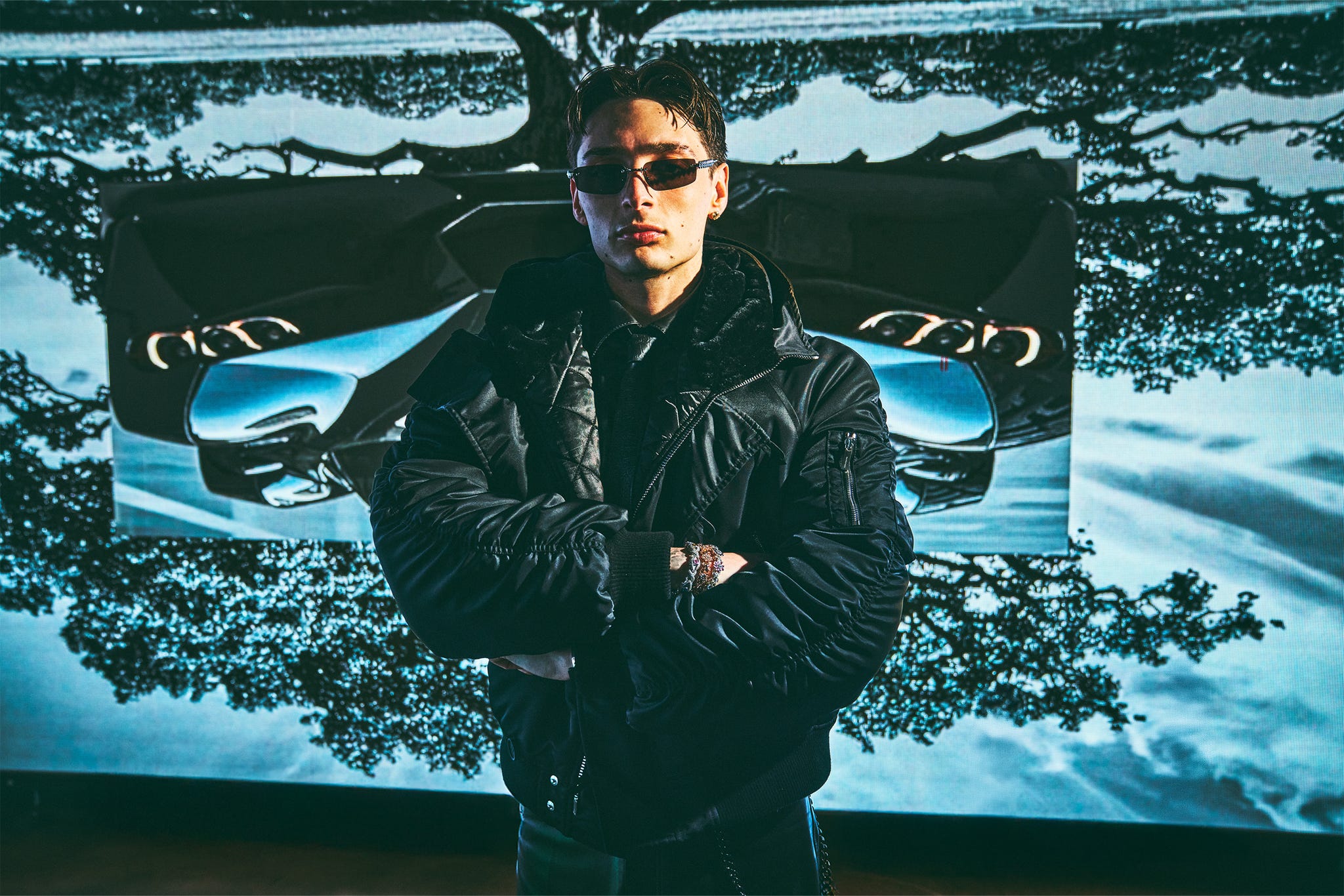 una persona posa con sicurezza davanti a un grande display digitale raffigurante un'auto ed elementi artistici