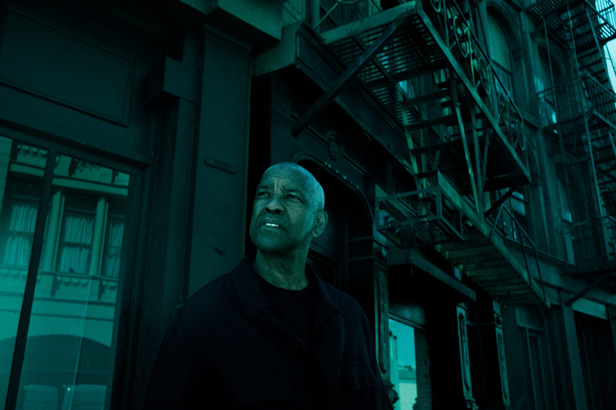 a person standing outside a building with a fire escape in a dimly lit urban setting