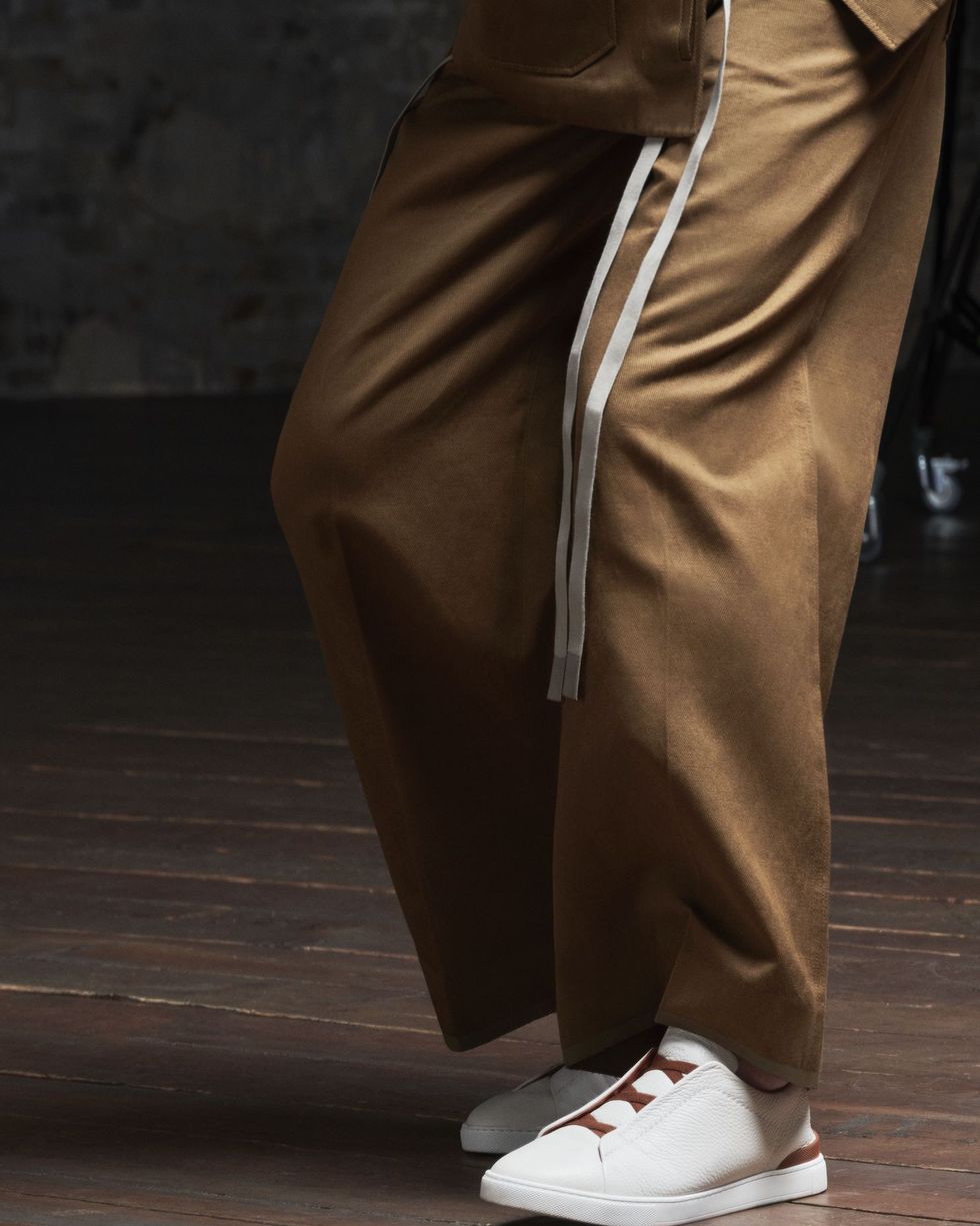 man waist down in brown trousers and white sneakers