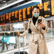 essential travels during lockdown   woman with face mask checking in online while waiting near arrival departure board