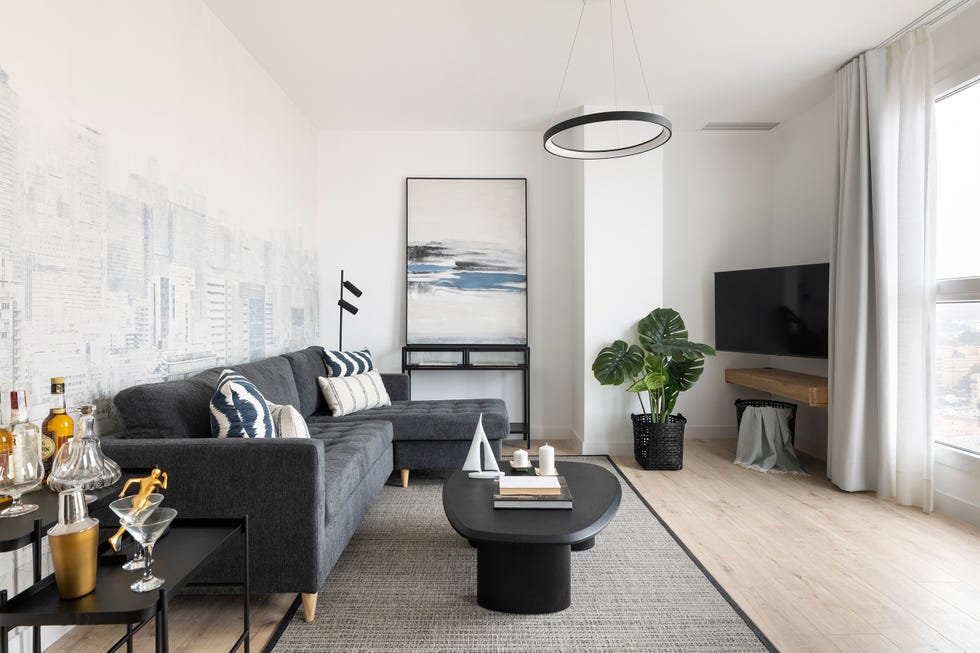 sofá con chaiselongue gris, mesa de centro negra y papel pintado con dibujos de edificios