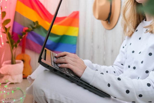 una chica escribe en el ordenador con una bandera lgbt de fondo