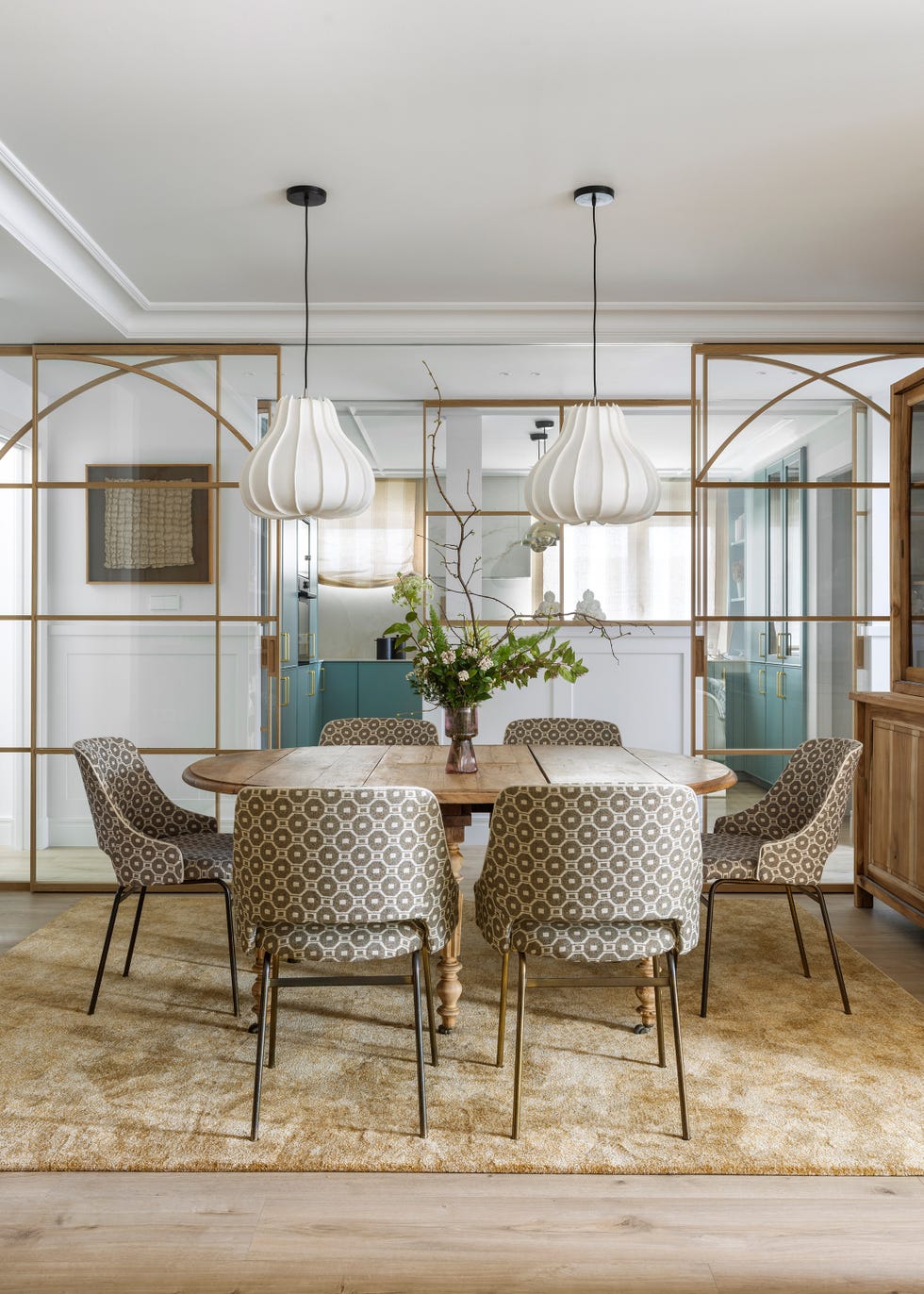 mesa de comedor ovalada de madera, sillas con tapizado geométrico y lámparas suspendidas