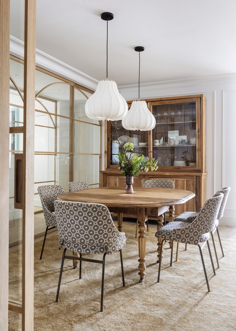 mesa de comedor ovalada de madera, sillas con tapizado geométrico y lámparas suspendidas