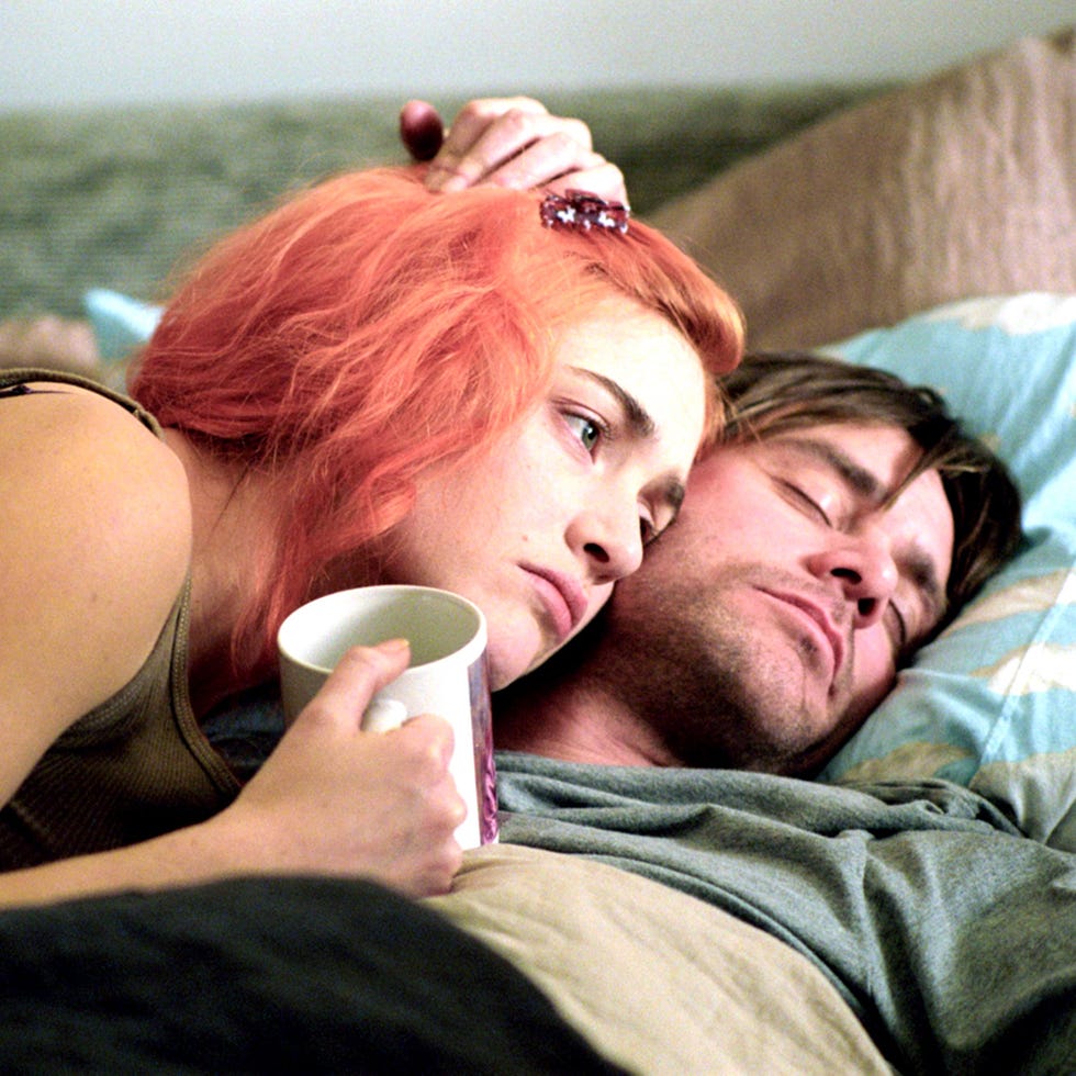 a person with vibrant red hair leans over another individual while holding a white mug a person with vibrant red hair leans over another individual while holding a white mug