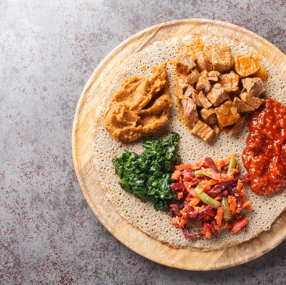 ethiopian injera topped with meat, vegetables, greens close up on the wooden board horizontal top view
