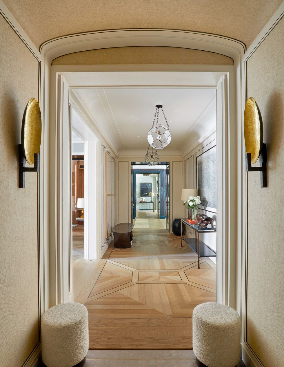 a cream colored entry with detailed parquet flooring and a pair of flat gold colored sconces