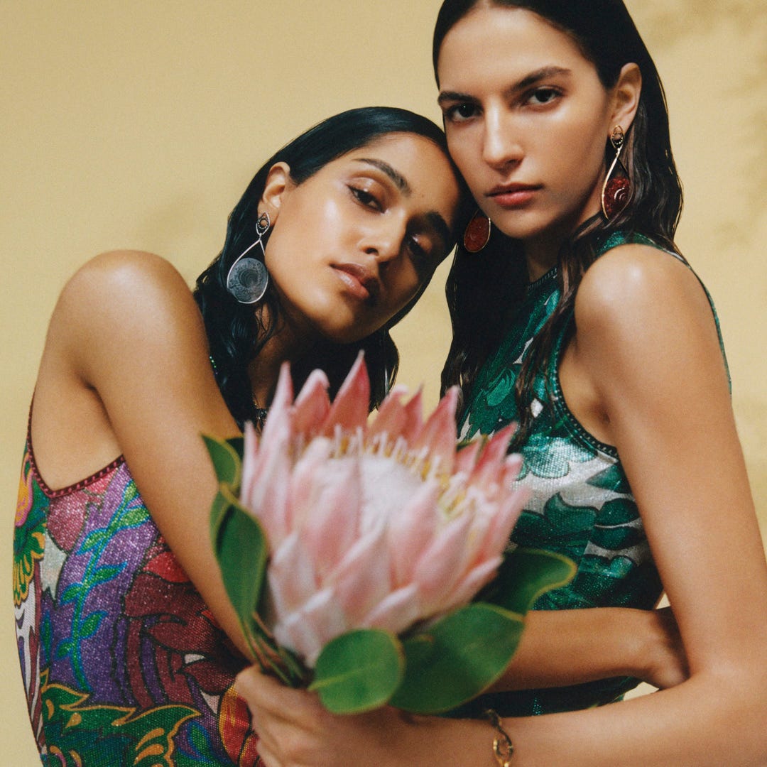 close up of two models in colorful dresses holding a large flower