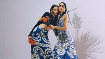 two models in vibrant blue patterned dresses holding flowers
