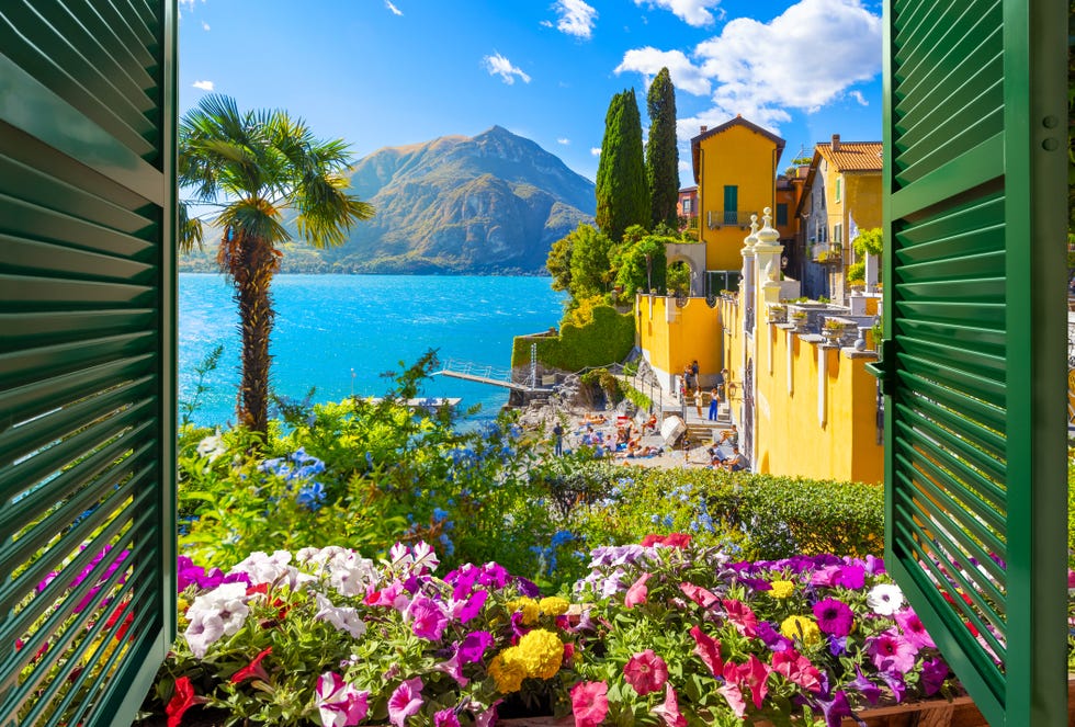 view through an open window with shutters looking down on the blue water and colorful picturesque resort village of varenna, italy, on the shores of lake como at summer