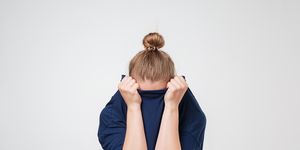 European woman hiding face under the clothes. She is oulling sweater on her head.