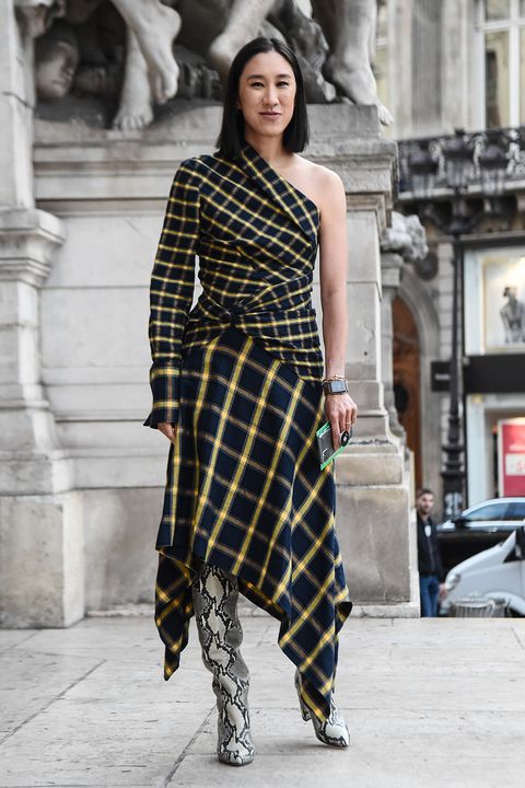 eva chen stands in front of a marble statue in the city wearing a plaid one shoulder dress with an asymmetrical hem in black and yellow along with snakeskin boots