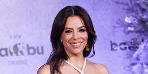 eva longoria smiles with her dark hair worn down and with a cream shoulderless dress with a neck strap