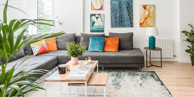 salón abierto con sofá en l gris con cojines de colores, paredes blancas decoradas con cuadros y una palmera