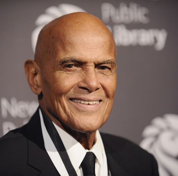harry belafonte looks toward the camera and smiles, he is wearing a black suit with a white shirt and black tie