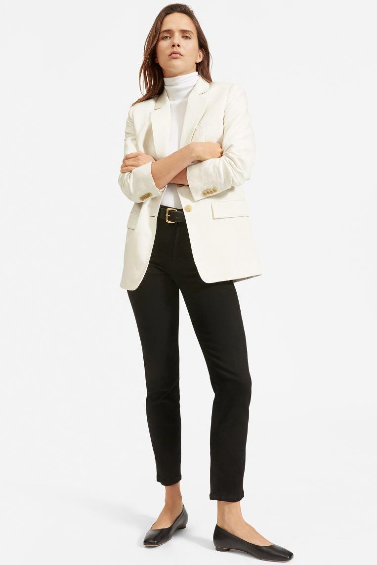 a model with her arms crossed wearing a white blazer, black pants, and black flats from everlane, good housekeepings pick for the best transparent sustainable clothing brand