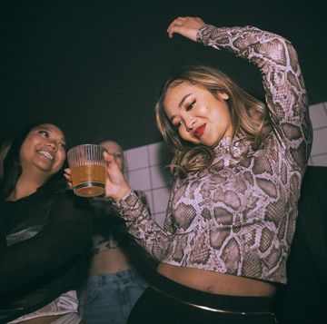 carefree young woman with drink dancing by female friend enjoying at nightclub