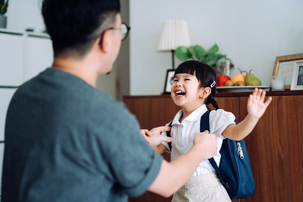 excited and happy little asian school girl getting dressed with her father in the living room and preparing for her first day at school