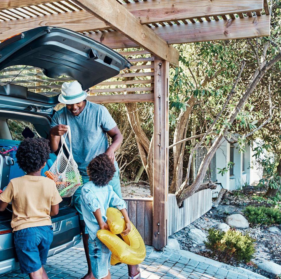 excited black family packing their car trunk for a trip to the beach. happy single dad and playful kids loading their boot for a summer vacation. time to travel and have fun on a road trip together