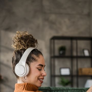 excited young woman listening to music on wireless headphones over a mobile app while sitting on a comfortable sofa